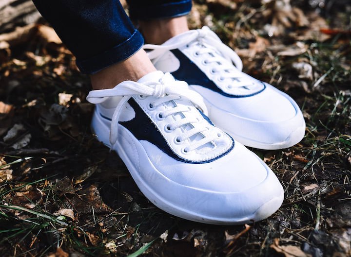 A side view of a pair of feet outside on grass wearing Groundies Performance Flow barefoot sneakers in white leather