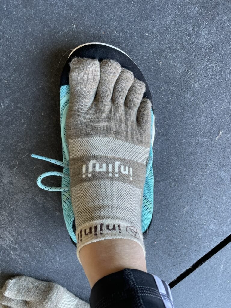 A woman's foot in injinji toe socks on top of a Xero Shoes 360 cross training shoe to show shape