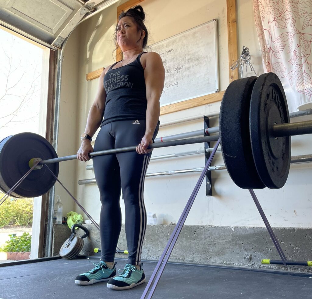 A woman holding lifting a heavy bar weight while wearing Xero Shoes 360 barefoot cross training shoe