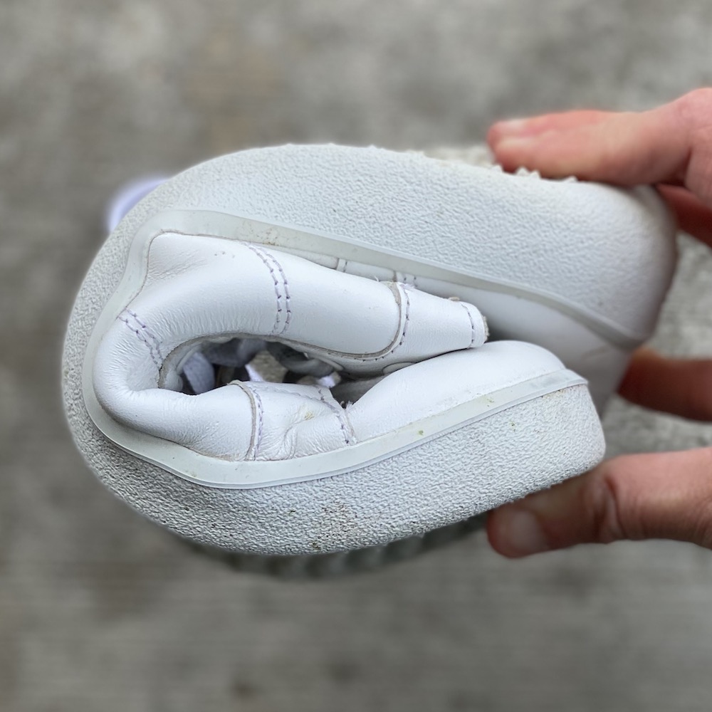 A close up of a hand holding a rolled up Be Lenka barefoot sneaker showing how flexible it is