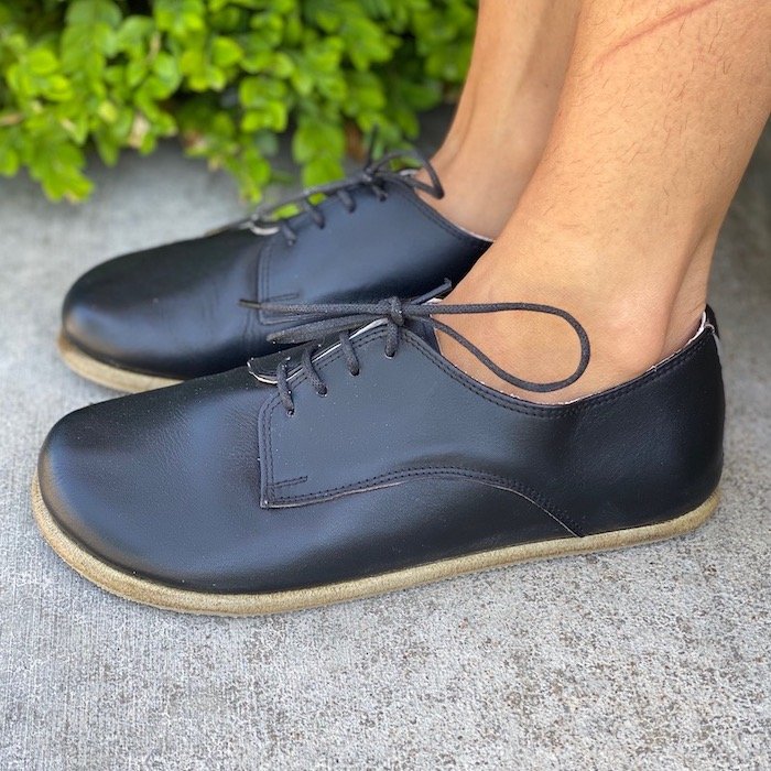 close up view of a pair of feet standing on pavement from the side wearing black leather barefoot oxfords by FeelBarefoot Aintap shoes