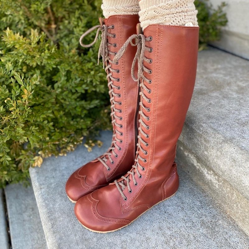 Side angled view of NoNs brogue tall brown leather lace up barefoot boots with zero drop sole and wide toebox