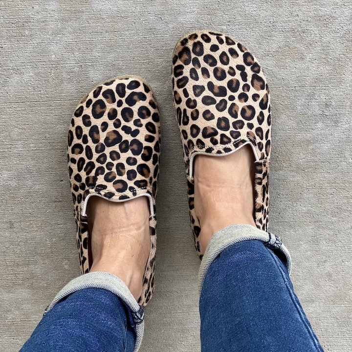 A top down view of a pair of feet standing on pavement wearing cuffed jeans and leopard print calf hair barefoot loafers in a natural foot shape from Anya's Shop - The Yasemin