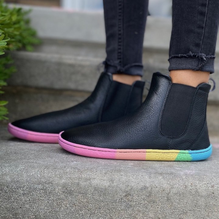 a side view of a pair of feet standing on concrete wearing PaperKrane barefoot chelsea boots rainbow Skitts