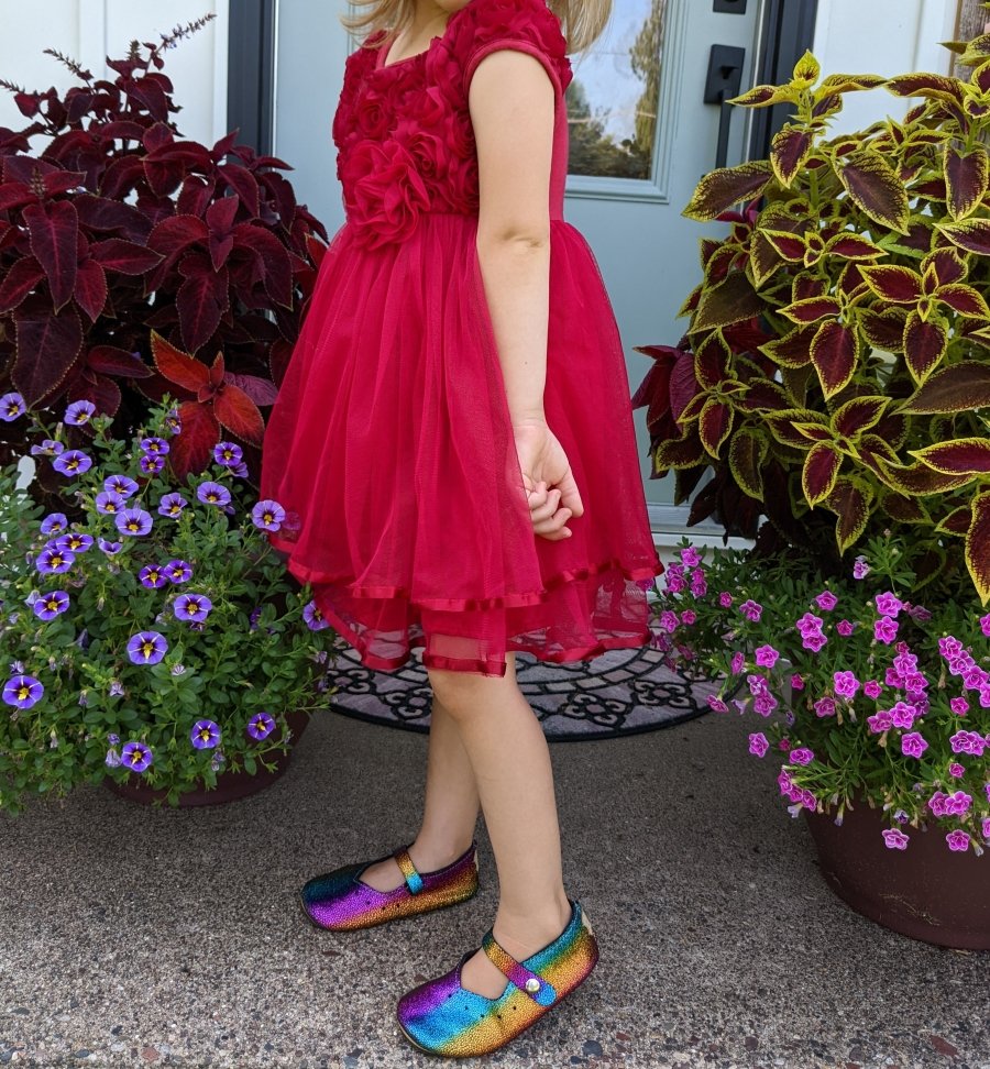 Photo from the neck down of a little girl in a red dress wearing Duchess and Fox rainbow mary janes