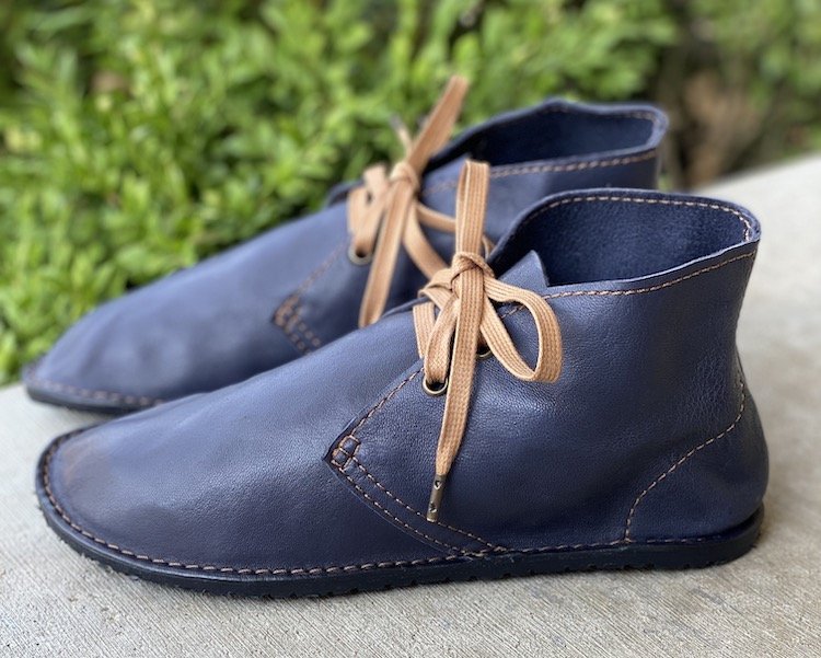 A close up side view of a pair of blue leather Barefoot Pals shoes with gold stitching and laces