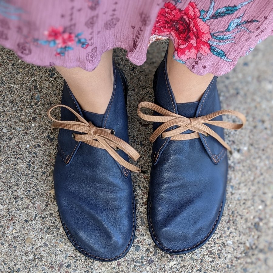 Top down close up of Navy leather super lightweight Barefoot Pals by Gaucho Ninja desert boots with gold cotton laces worn by a woman with extra wide feet. Her lavender flowy skirt is visible at the top of the frame