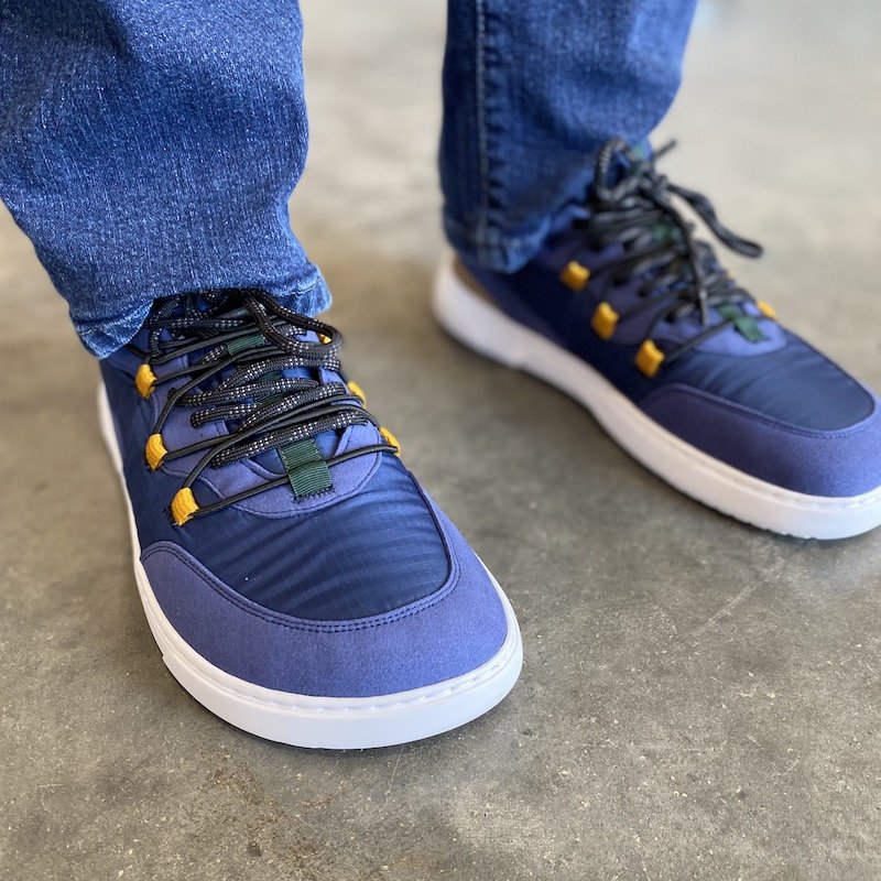 a close up of a pair of feet standing on concrete wearing blue Revive Barebarics barefoot chunky sneakers