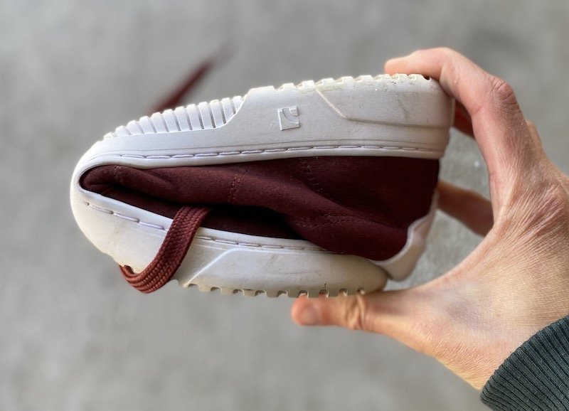 a close up of a hand holding a rolled up barebarics zero drop barefoot sneaker to show its flexibility