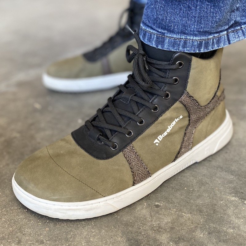 a close up of a pair of feet standing on concrete wearing jeans and green Hifly Barebarics hightop barefoot sneakers