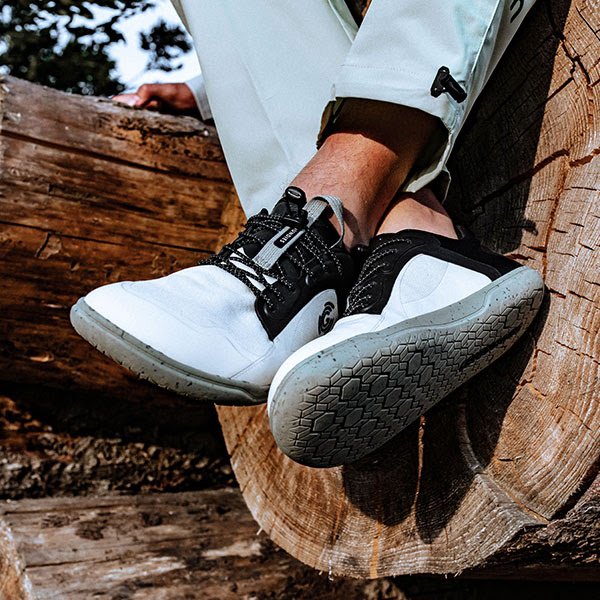 Groundies Active sports shoes on zero drop outsole being seen worn with someone crossing their legs against a log