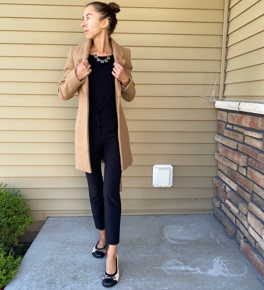 A photo of a woman wearing all black with a camel coat and groundies felicia barefoot ballet flats in beige with a black toe cap