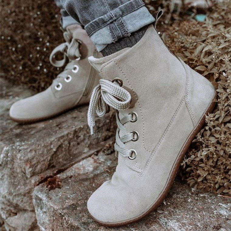 Groundies Salzburg close up side view of a person wearing them on stone, flexing one foot up. They feature large eyelets, thick laces, and soft nubuck on a zero drop flexible outside with wide toe box