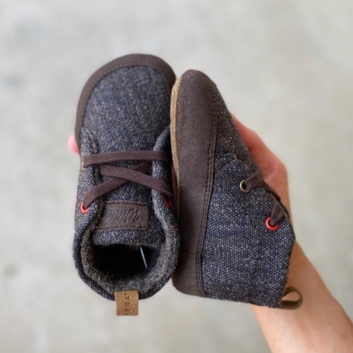 A hand holding an adorable pair of tiny Wildling Chestnut wool barefoot booties for littles. They are the cutest shoes ever.