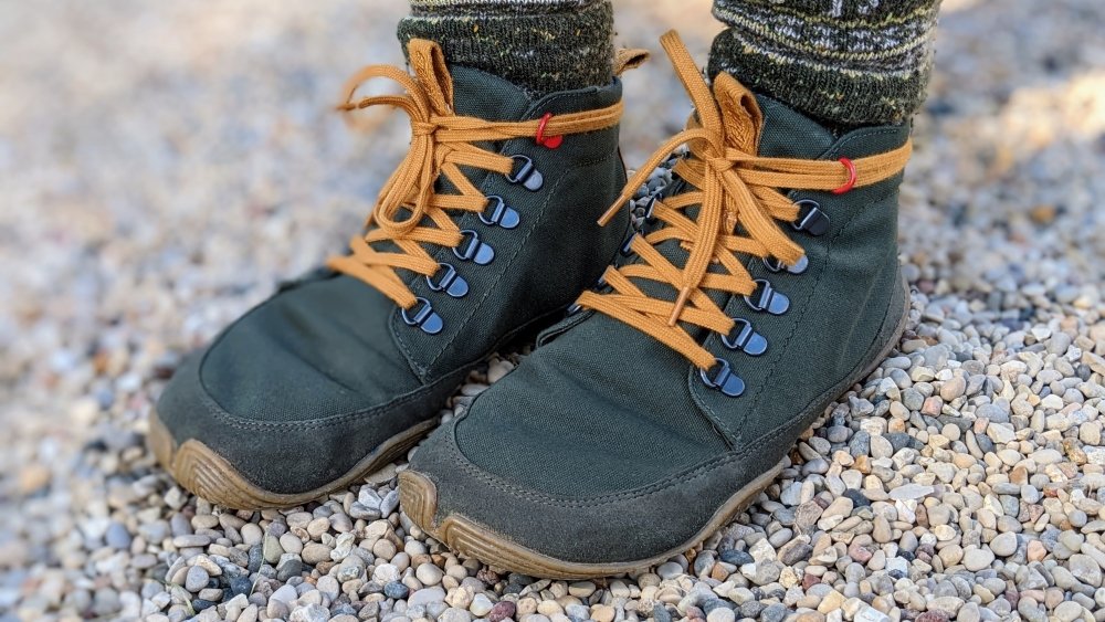 Close up of Wilding Yew worn with socks on small rocks. They are olive green dense weave canvas with wool interior and very flexible outsole with anatomical toe box