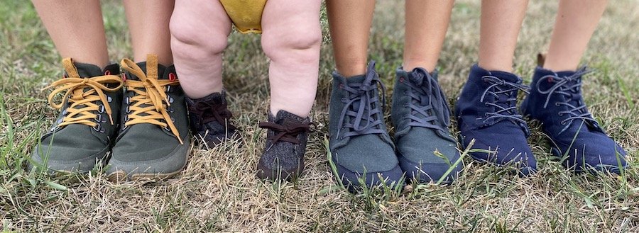 Wildling Shoes Autumn Winter models being worn by 4 people. The picture is from the shins down, and there's a chubby baby being held standing in the middle. Yew, Chestnut, Chokeberry, and Pine models are represented