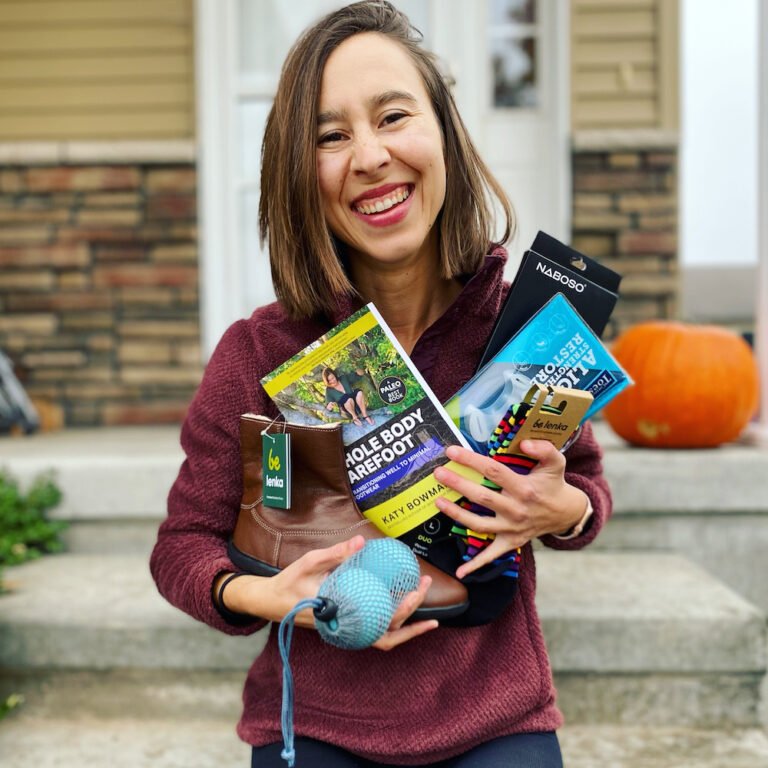 A woman holding a pile of healthy foot gear and barefoot shoes and socks