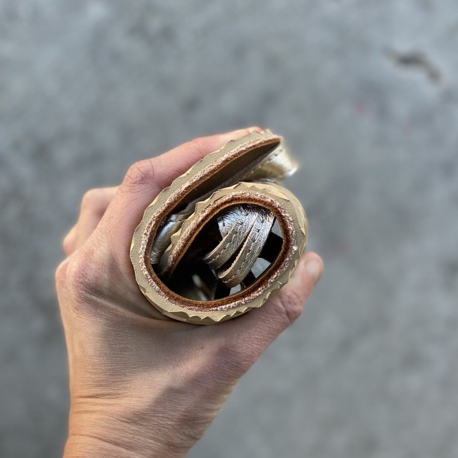 Close up of a hand holding a rolled up Jenon Leather sandal to show flexibility. The sandal easily rolled into a tight spiral with a flexible zero drop outsole