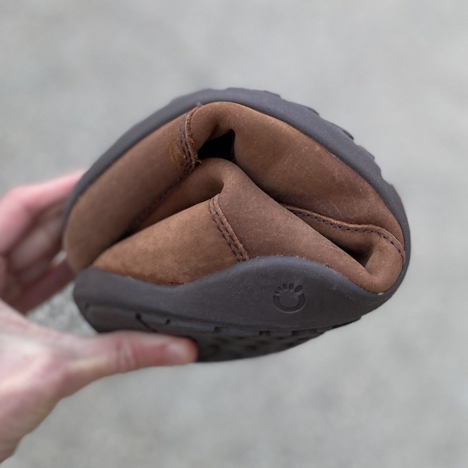 A close up of a hand holding a rolled up Xero Shoes barefoot Boot to show its flexibility, the model name is Denver Leather