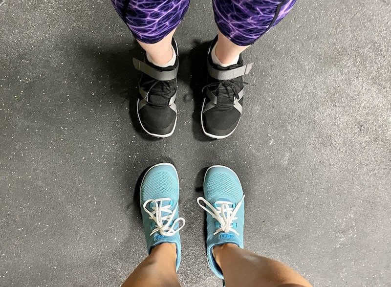 a top down view of two pairs of feet and legs facing each other wearing xero shoes Forza Trainer and Forza Runner barefoot athletic shoes