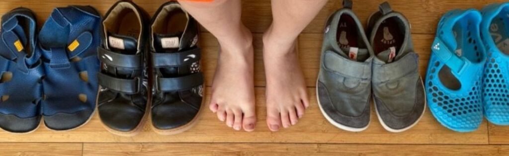 a row of kids barefoot shoes on the floor next to a pair of a child's bare feet