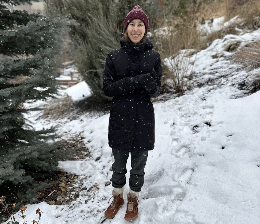 a woman standing outside among trees with snow falling wearing Be Lenka barefoot winter boots Bliss