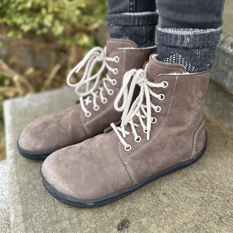 A close up of a pair of feet standing on wet concrete wearing Be Lenka Winter 2.0 barefoot boots in chocolate brown