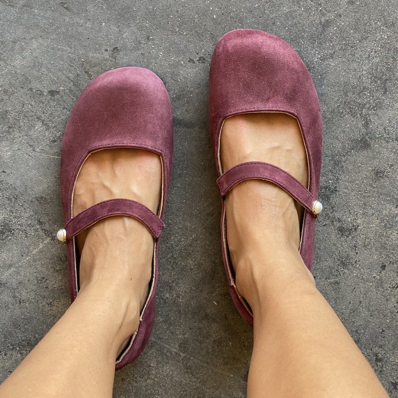 A top down view of a pair of feet standing wearing burgundy Lisbeth Joe Paris barefoot mary janes