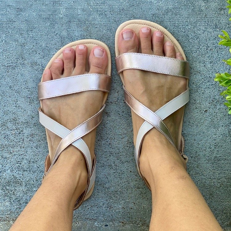 A top down view of a pair of feet standing on concrete wearing Shapen Barefoot Calla Sandals in Rose gold