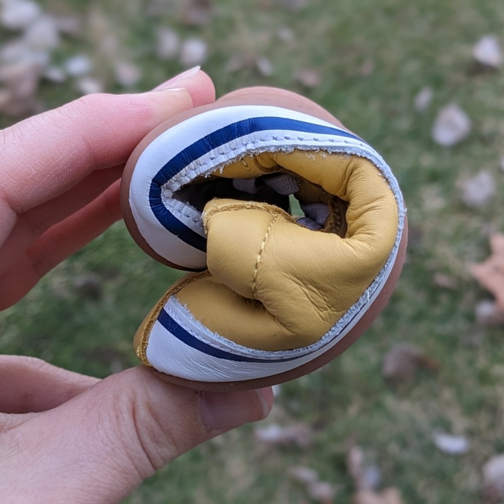 A hand holding a toddler Tip Toey Joey shoe into a tight roll showing the flexibility