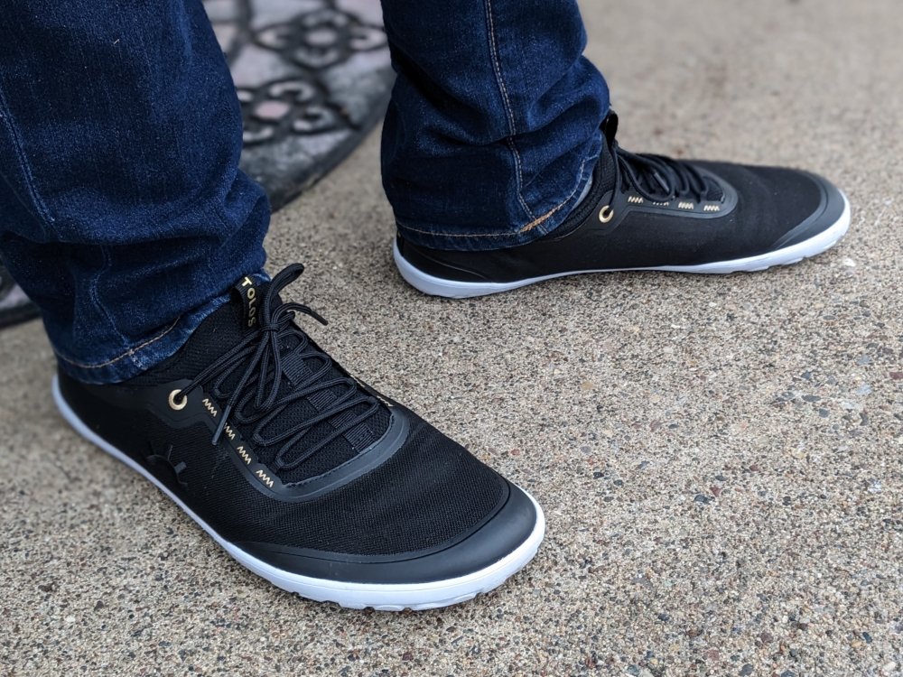 Close up of black Tolos barefoot athletic sneakers with gold accents being worn