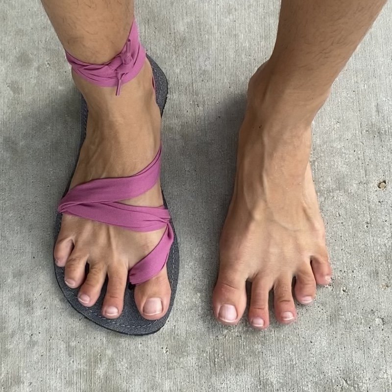 A top down view of a pair of feet, one is bare and the other is wearing pink stylish barefoot sandals for women from Juuri