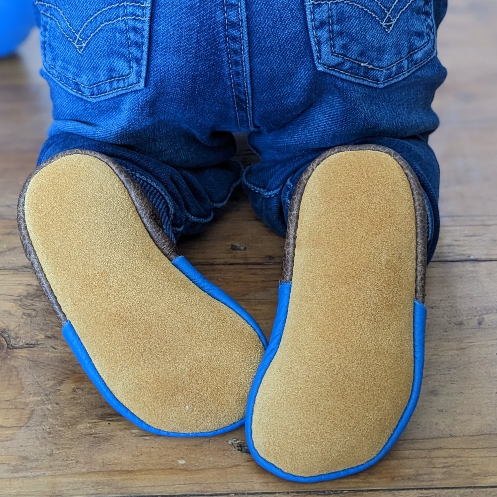 A close up of a baby crawling in jeans and softstar barefoot moccasins outsole is prevalent in the photo. You can see the wide toe box for proper foot developement