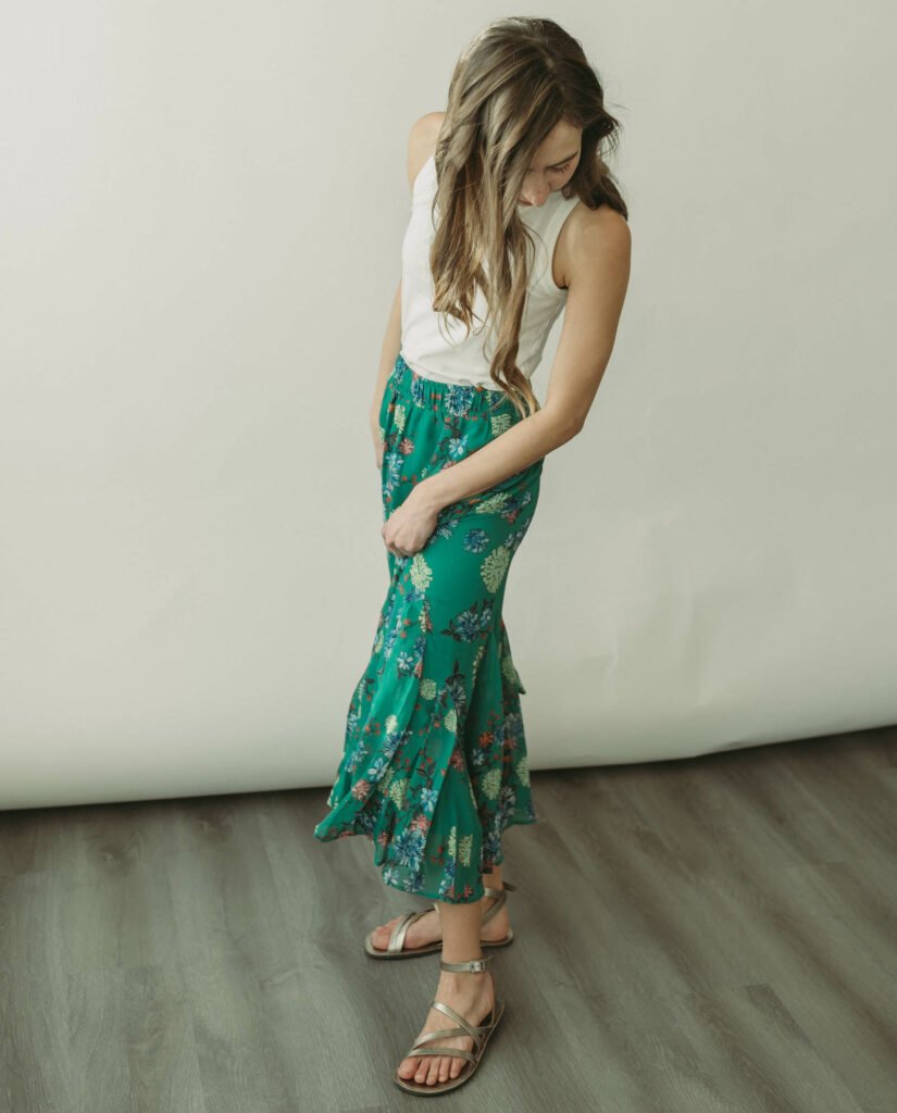 A woman wearing a long green skirt and Groundies stylish barefoot shoes, the Florence sandal in bronze