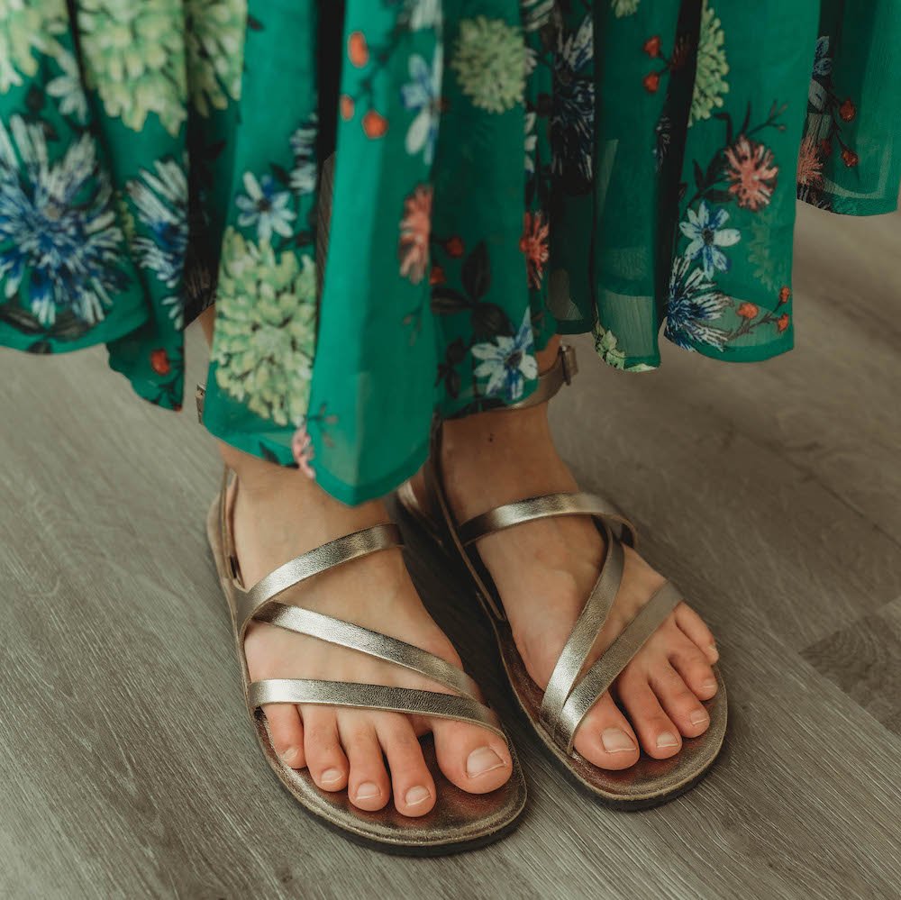 A close up of a woman wearing Groundies Florence stylish barefoot sandals in bronze with a green floral skirt