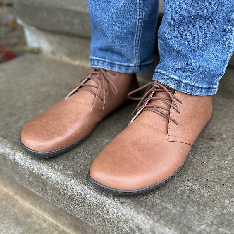 A man standing on concrete wearing brown Groundies Milano desert boots, barefoot dress shoes for men and women