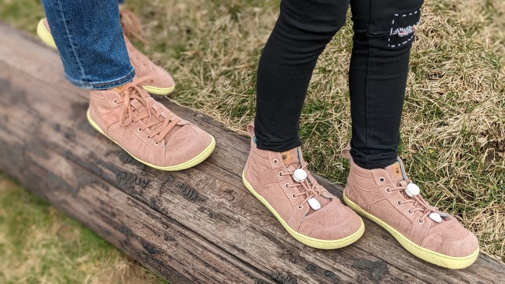 Two people wearing Mukishoes Hope Sustainable natural barefoot shoes walking on a log. The child is in front of the adult