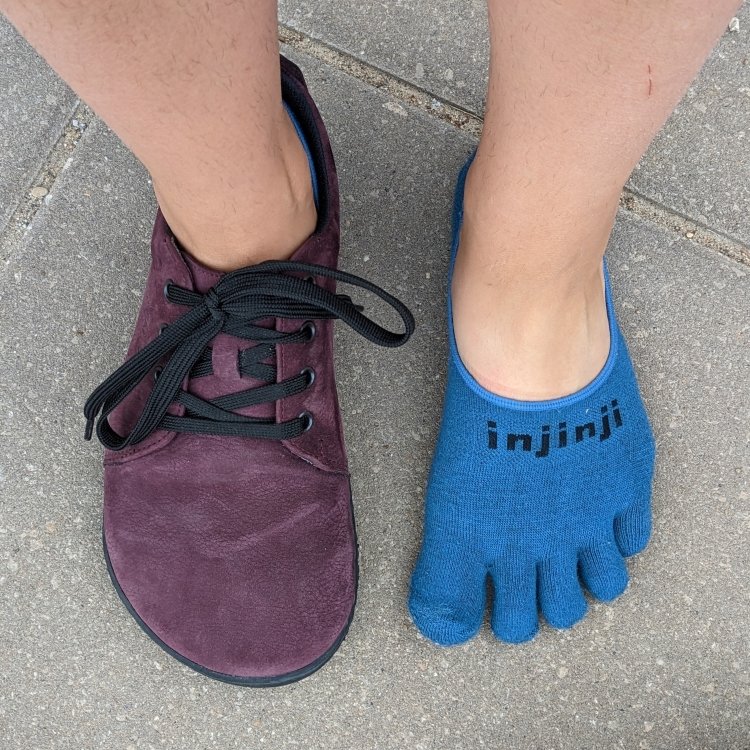 Top down close up of a pair of feet with 1 shoe off wearing just toe socks, and the other foot wearing Realfoot City Jungle extra wide toe box barefoot sneaker