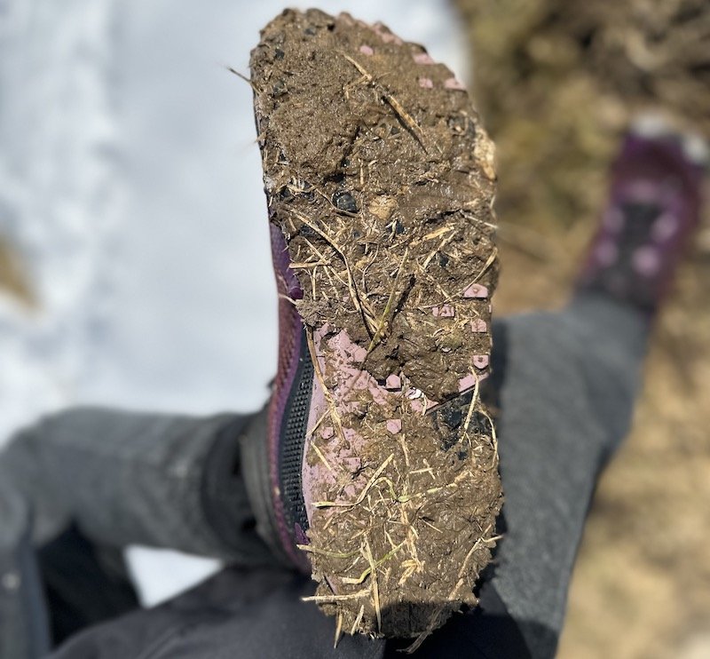 Close up view of a mud caked sole on Xero Shoes Scrambler Mid hiking boot. The outsole is full of rocks and mud and the wide toe box is visible