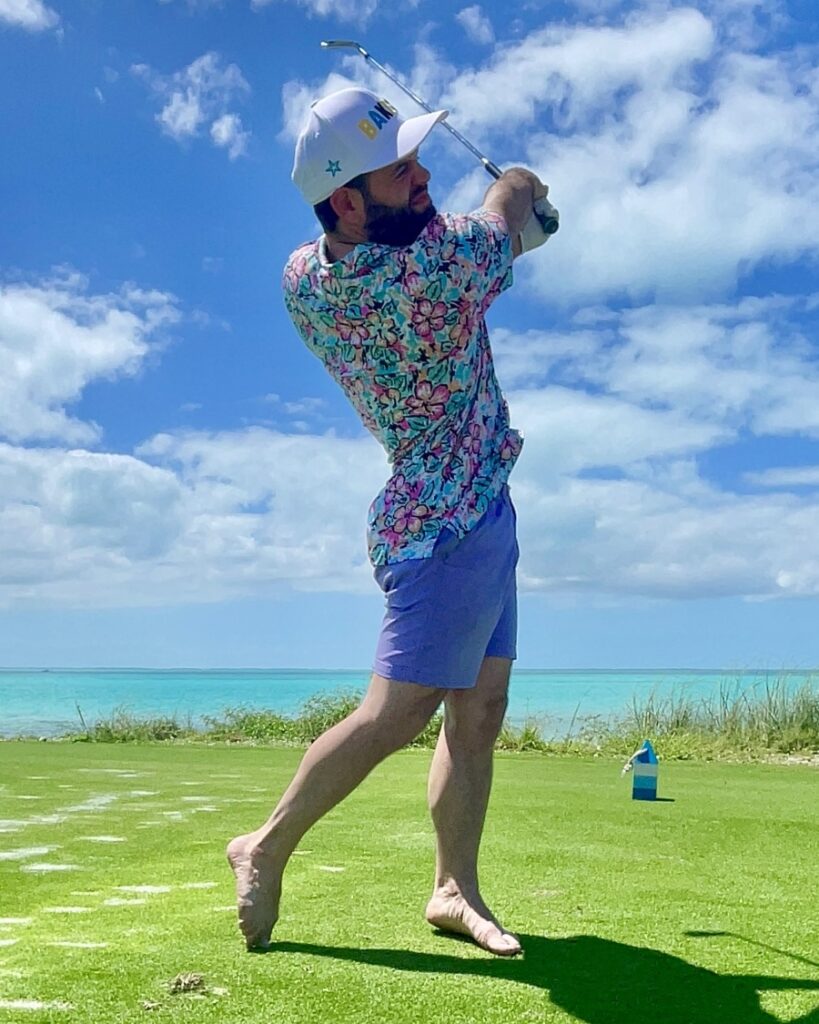 A photo of a man in shorts and colorful shirt golfing barefoot