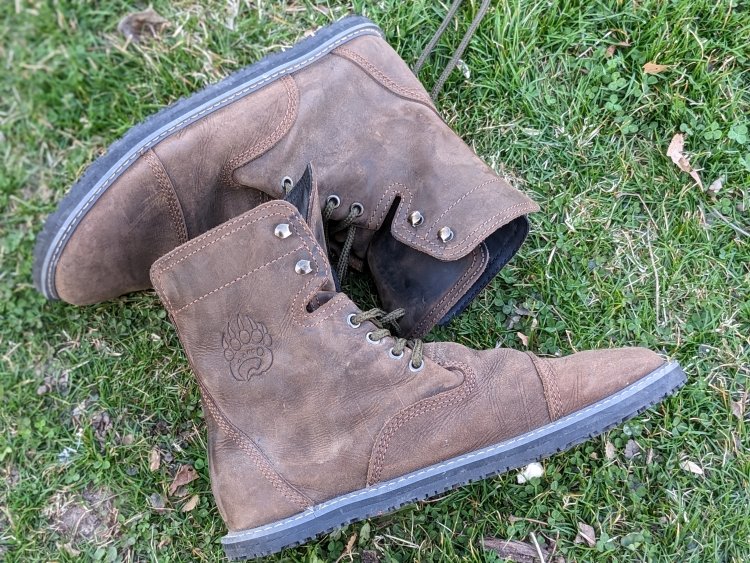 A pair of bearfoot shoes Bruin boots laying on their sides on the grass showing the thicker zero drop outsole and rugged leather uppers