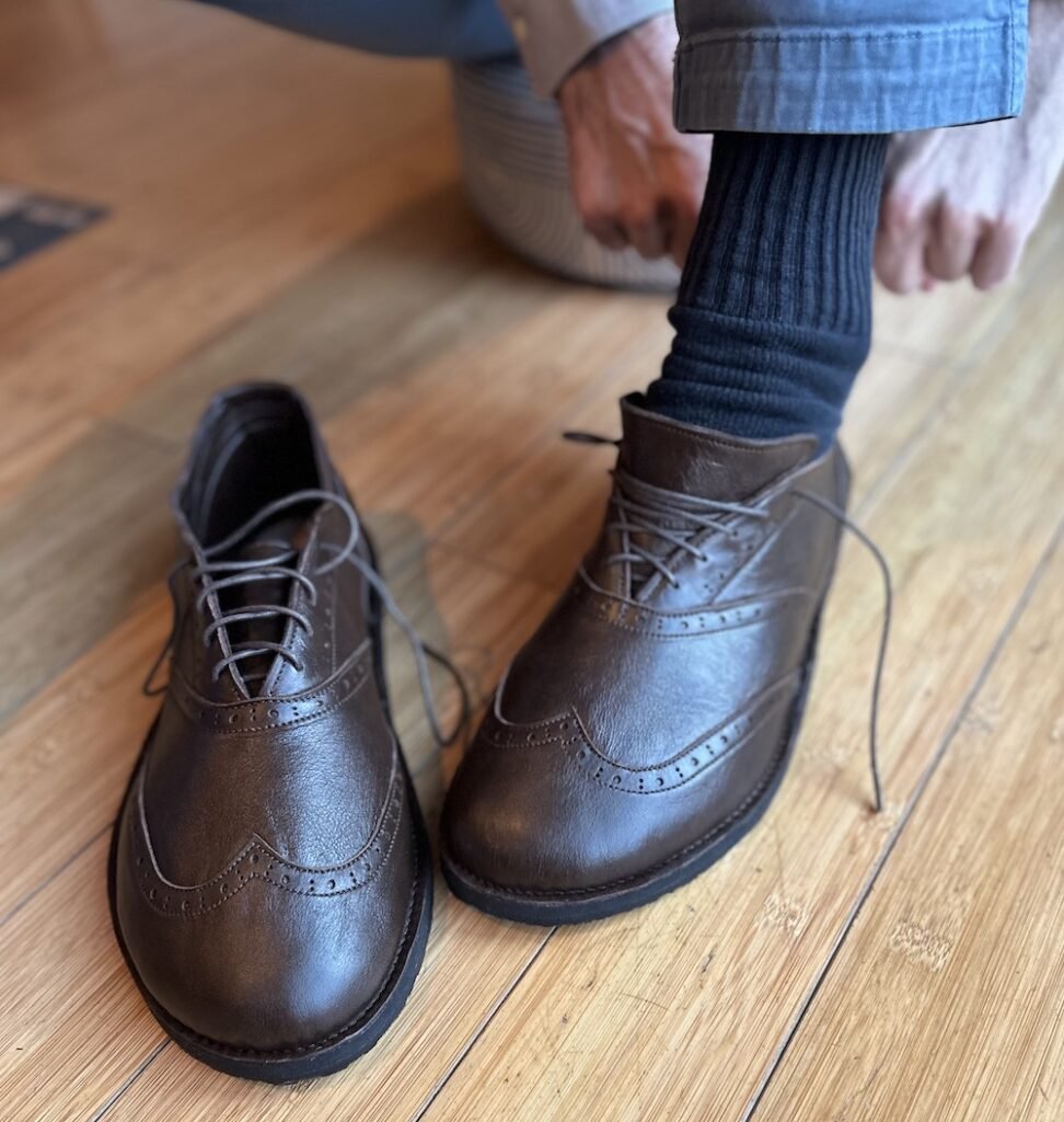 New Softstar Shoes oxfords, the Taylor wingtip brogue in brown is on the floor with a man putting his foot into one