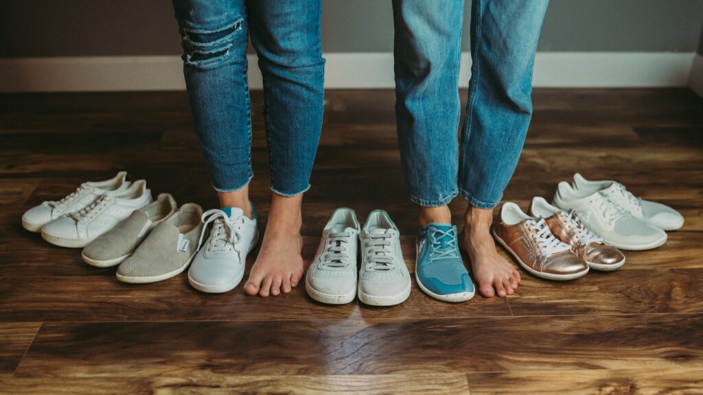 A thigh down straight on photo of two people in jeans standing with 1 bare foot and 1 foot in a barefoot shoe line up arranged in an arc