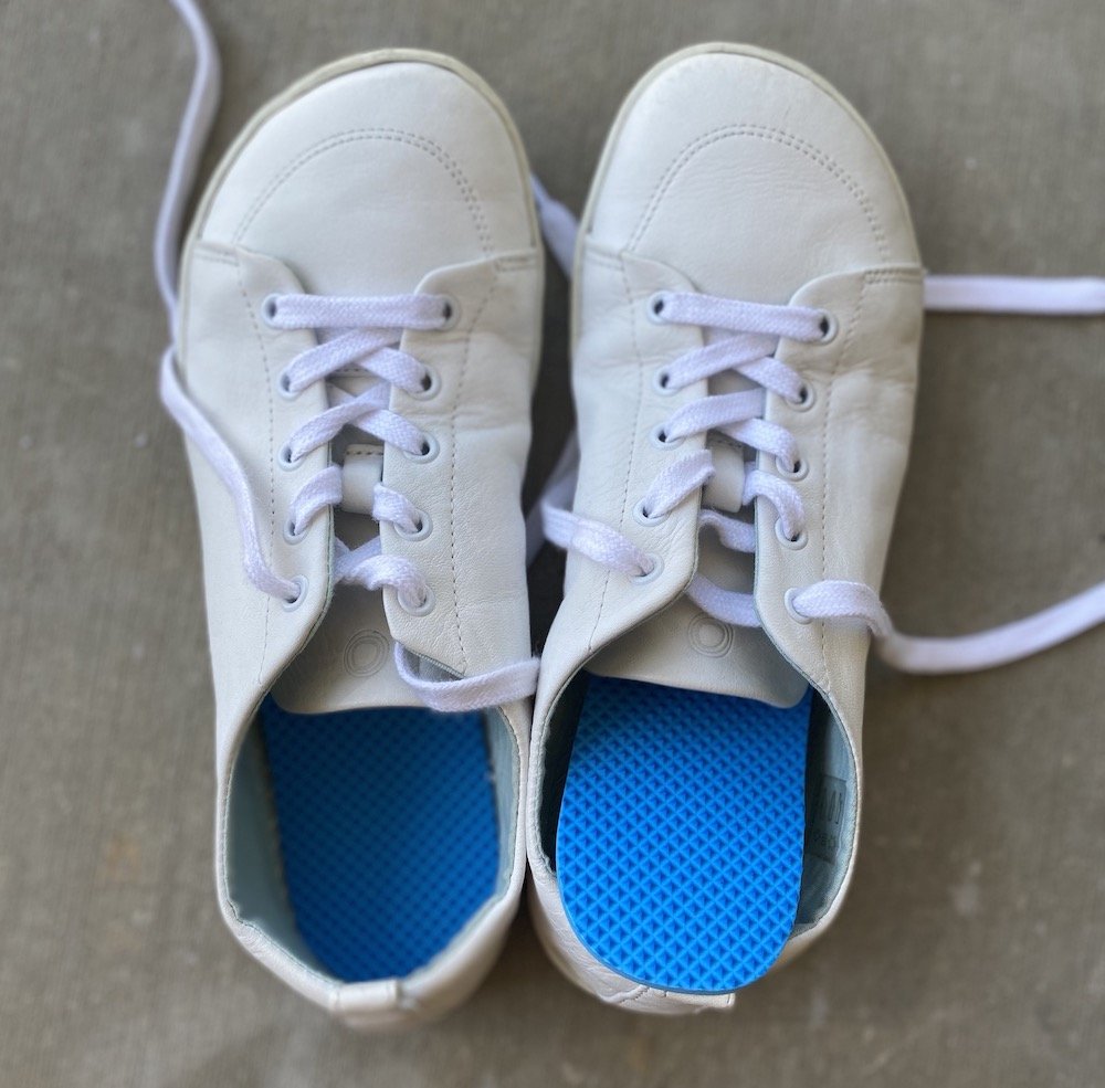 A top down view of a pair of white barefoot shoes with Naboso proprioceptive insoles visible inside the shoes