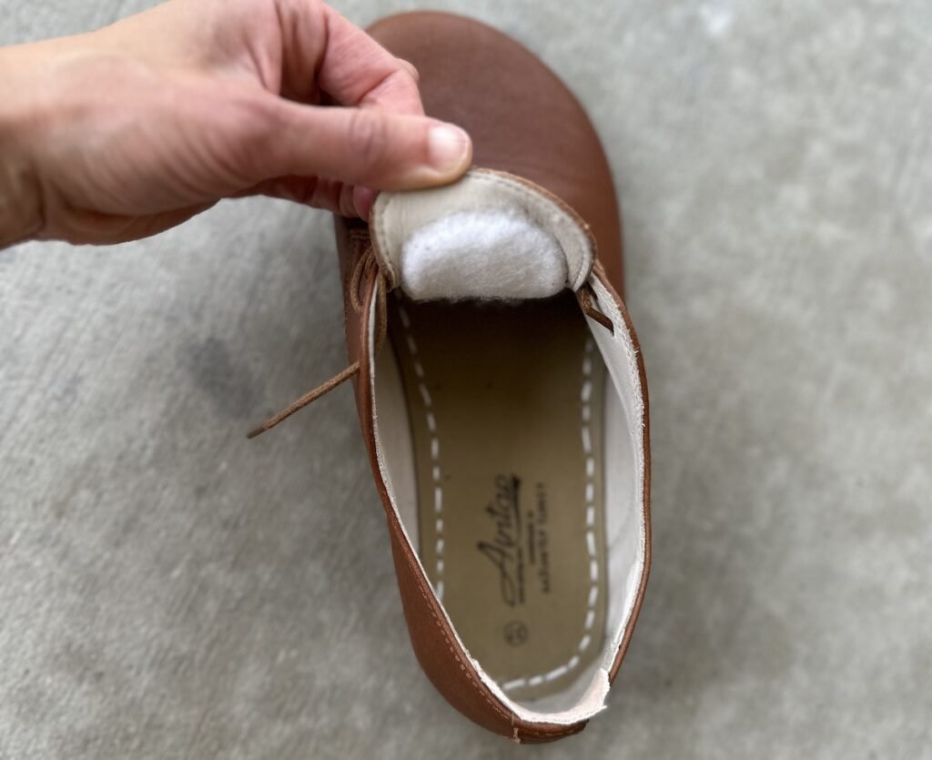 A close up of the inside of a shoe with the underside of the tongue lifted to show a felt tongue pad stuck to it to make the barefoot shoes fit better