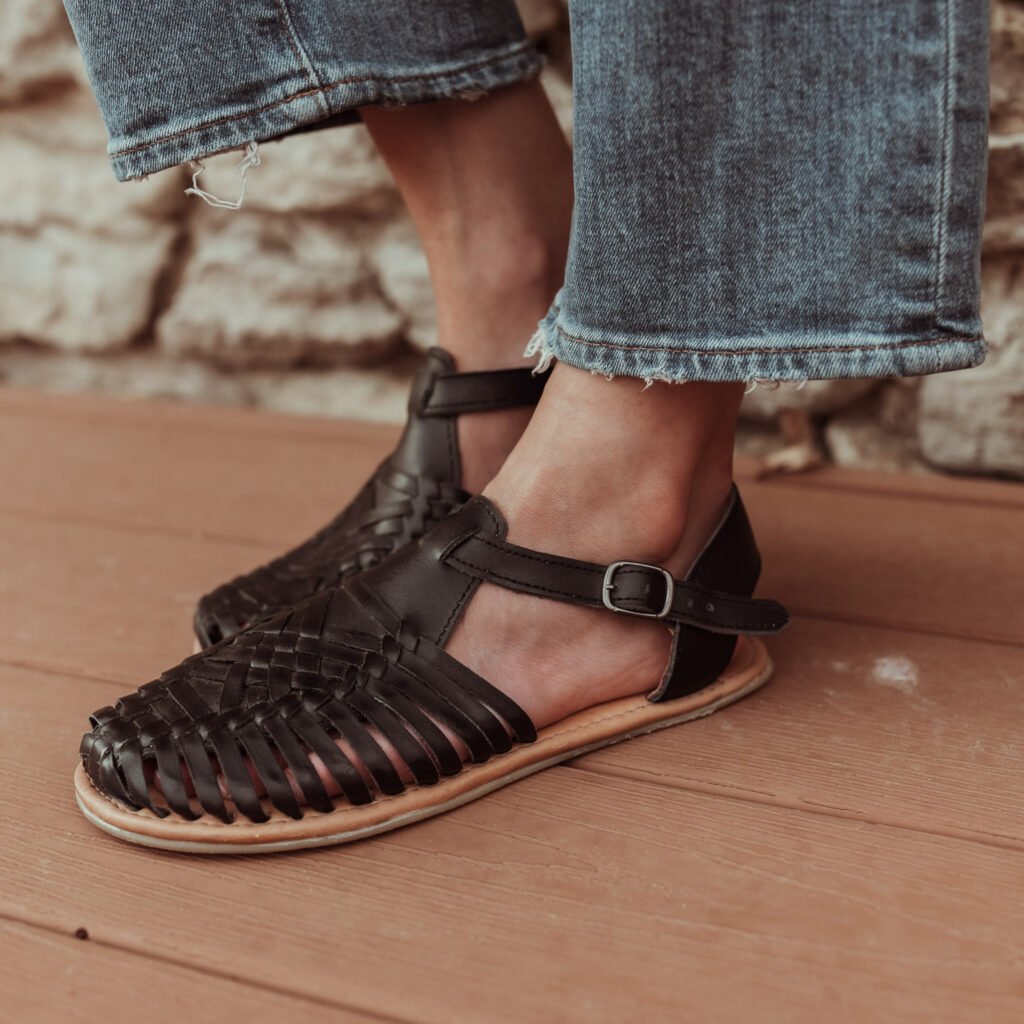 Close Up On Girl's Feet Wearing Black Sandals And Blue Jeans On