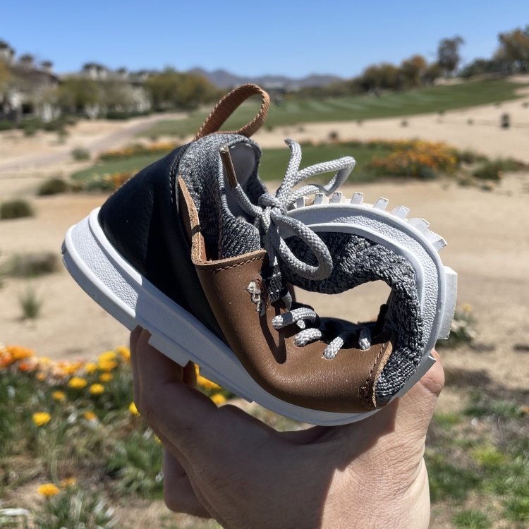 A hand holding up a True Linkswear Golf Shoe on a zero drop outsole rolled up to show the flexibility