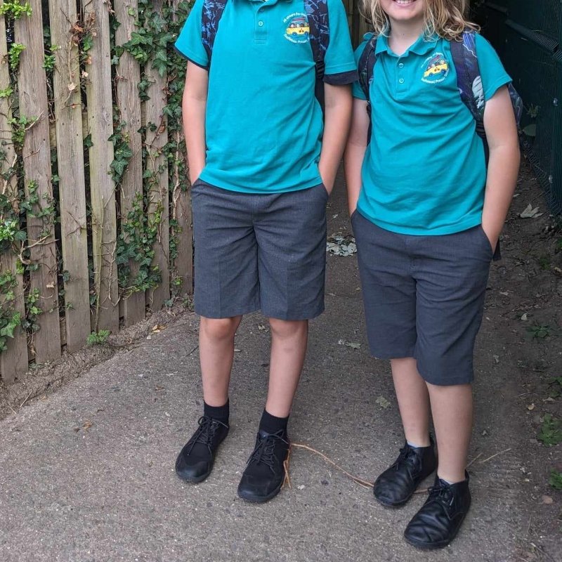 Two children shown from the neck down wearing school unforms and black barefoot shoes.