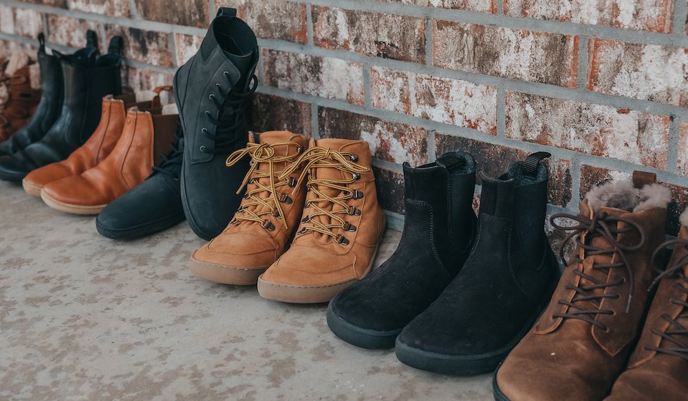 a row of barefoot boots for men and women lined up against a wall from different brands in black and brown.