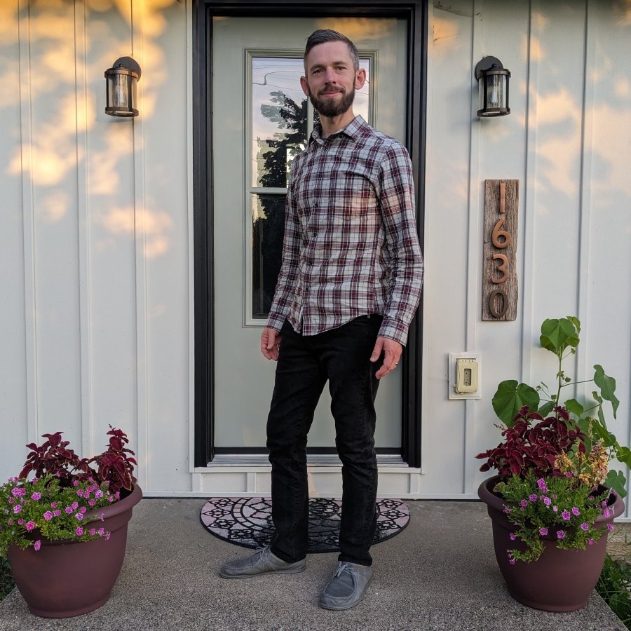 Full body photo of a man with graying hair and black jeans wearing gray magical Shoes cameron barefoot flexible dressy shoes with a plaid shirt. he is standing on his front steps slightly angled away from the camera